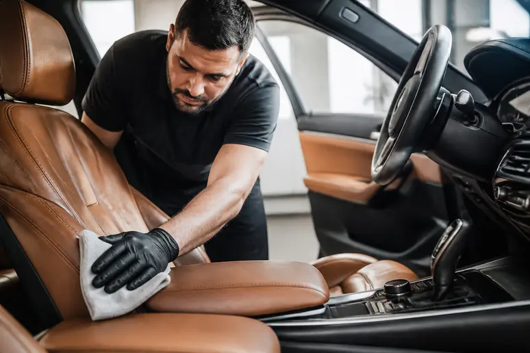 Application d'une lotion protectrice sur le cuir d'une voiture dans un atelier de detailing en France.