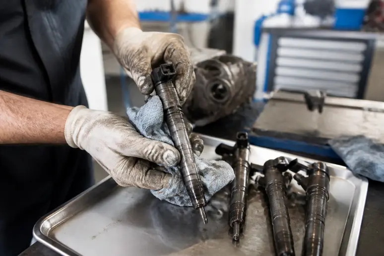Des mains de mécanicien nettoient des injecteurs de carburant dans un atelier automobile français.