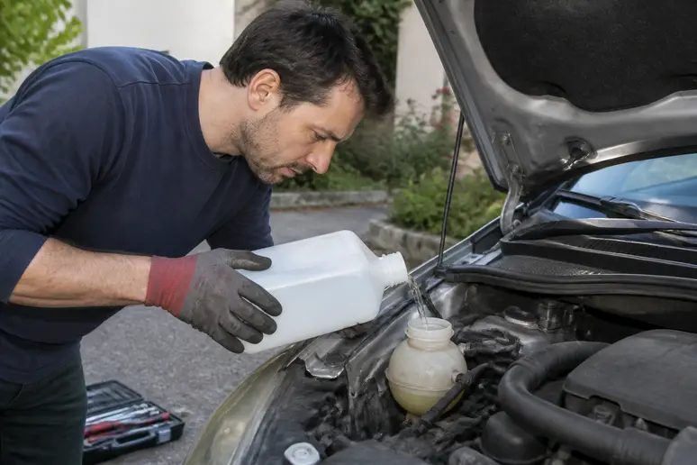 Un automobiliste français rince méticuleusement le circuit de refroidissement de son véhicule avec de l'eau propre.