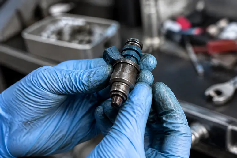 Mains gantées d'un mécanicien tenant un injecteur automobile pour un nettoyage des injecteurs.