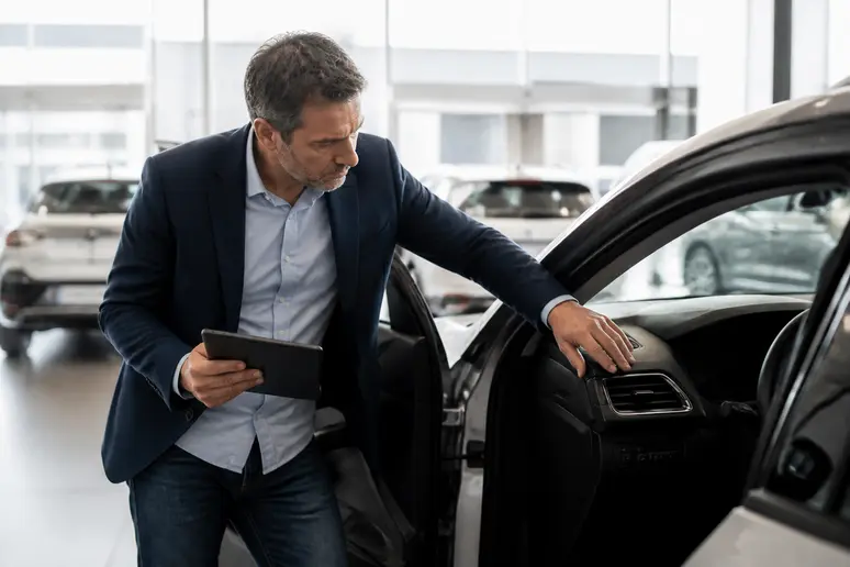 Un homme d'une cinquantaine d'années examine la planche de bord d'une voiture d'occasion dans une concession Spoticar lumineuse.
