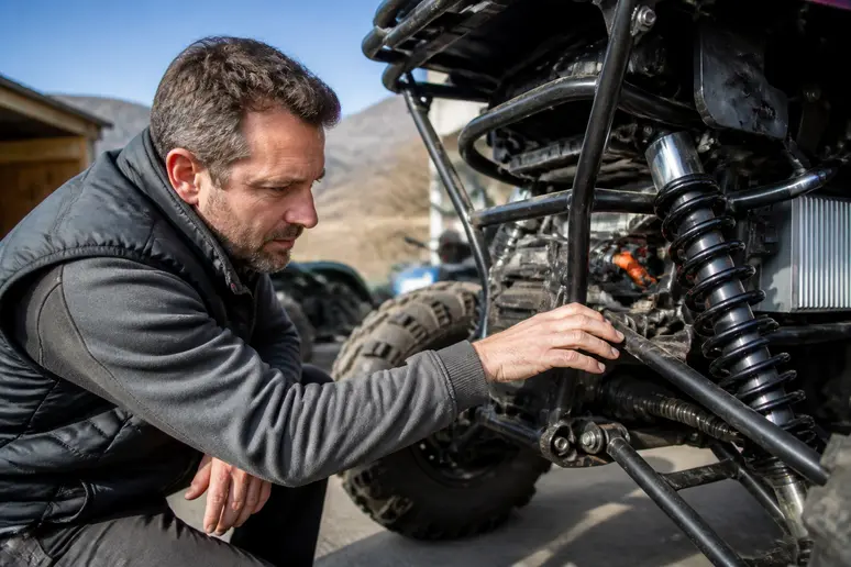 Un homme examine attentivement le châssis d'un quad electrique adulte sous le soleil.