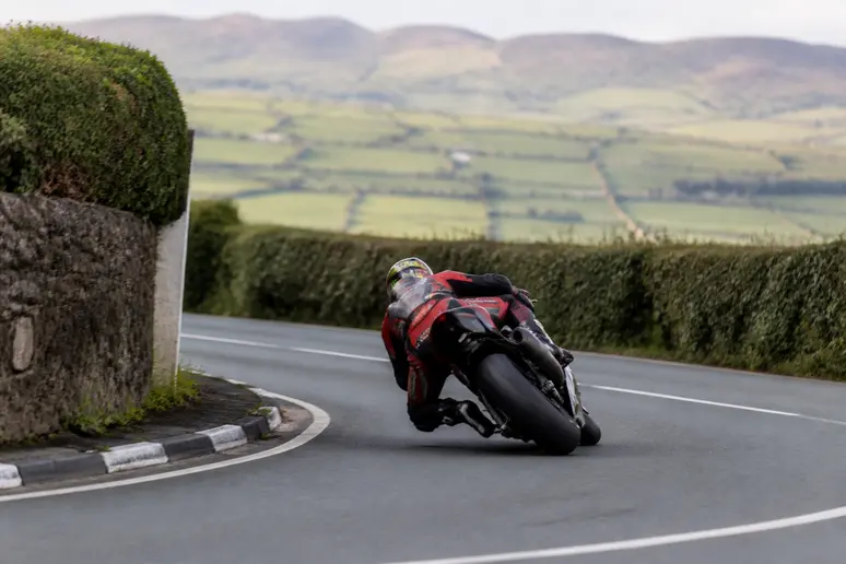 Vue d'un virage serré du Tourist Trophy, motos Superbike en pleine course, vitesse impressionnante, décor de l'île de Man.