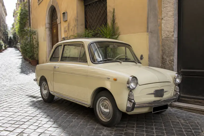 Autobianchi Bianchina stationnée dans une rue pavée européenne baignée de lumière naturelle