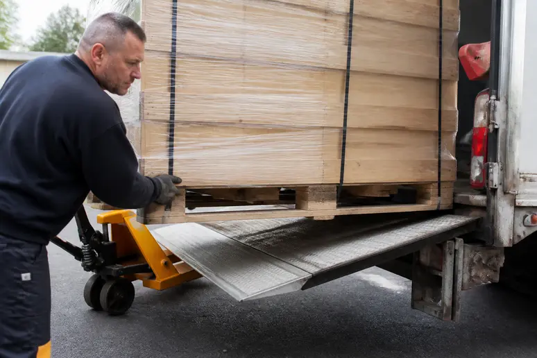 Manutentionnaire ajustant une palette lourde sur le plateau élévateur d'un camion