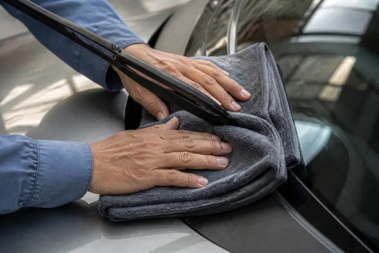 Bras métallique d'essuie-glace relevé au-dessus d'un chiffon de protection posé sur le pare-brise