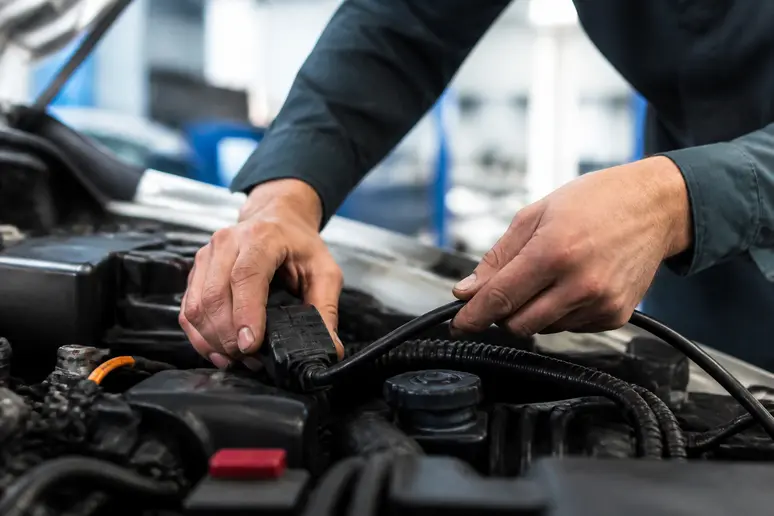 Un mécanicien connecte les câbles de diagnostic électronique dans le compartiment moteur d'une voiture.