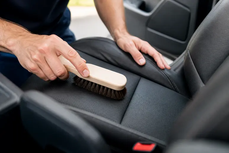Mains utilisant une brosse souple pour nettoyer un siège en cuir de voiture sans risque.