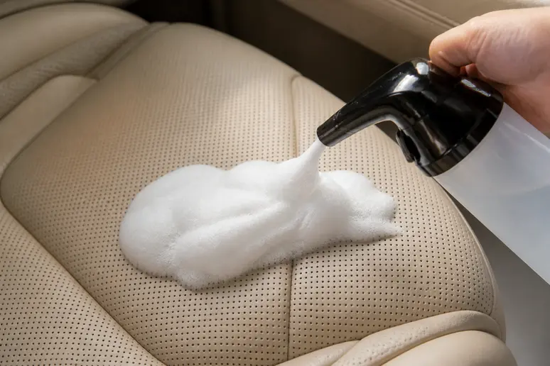 Application d'une mousse nettoyante sur le cuir perforé d'une sellerie automobile ventilée.