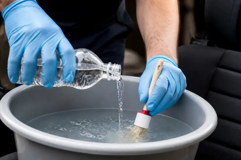 Mains gantées préparant le mélange de vinaigre et d'eau pour nettoyer un siège de voiture en tissu.