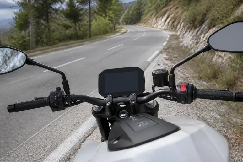 Guidon et tableau de bord d'une moto 125 électrique arrêtée sur le bas-côté d'une route.